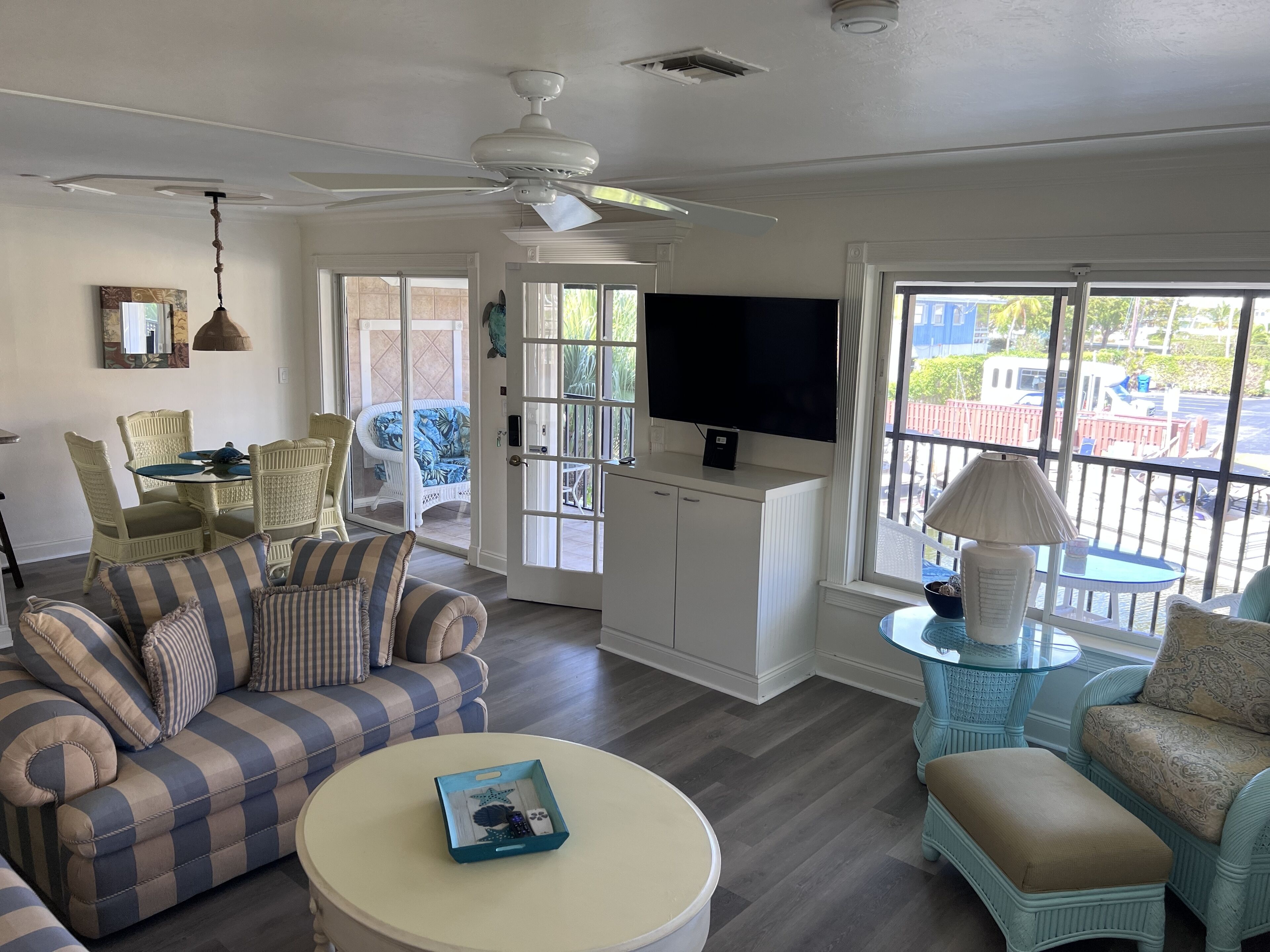 A living room with a striped sofa, a round coffee table, a television, and a balcony with a view of the outside.