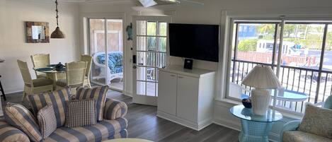 A living room with a striped sofa, a round coffee table, a television, and a balcony with a view of the outside.