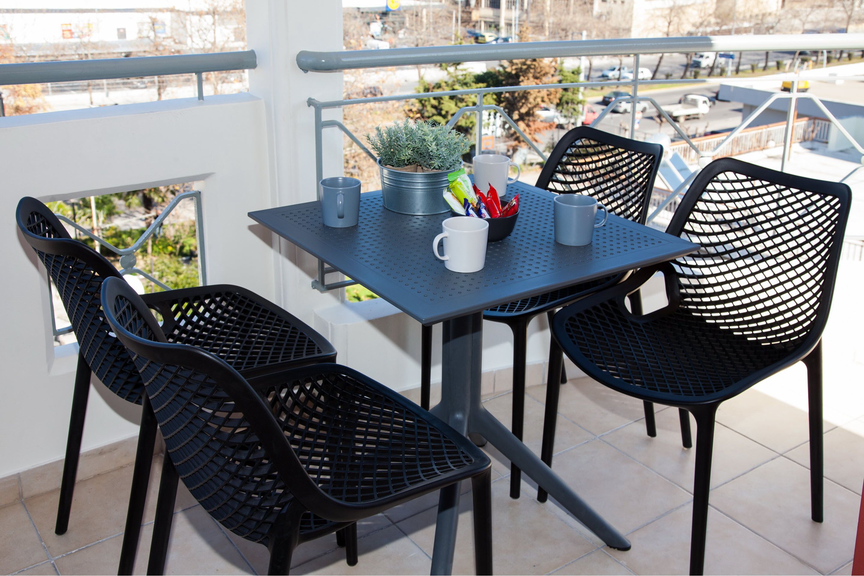 A balcony with a table and chairs, a potted plant, and a view of a parking area.
