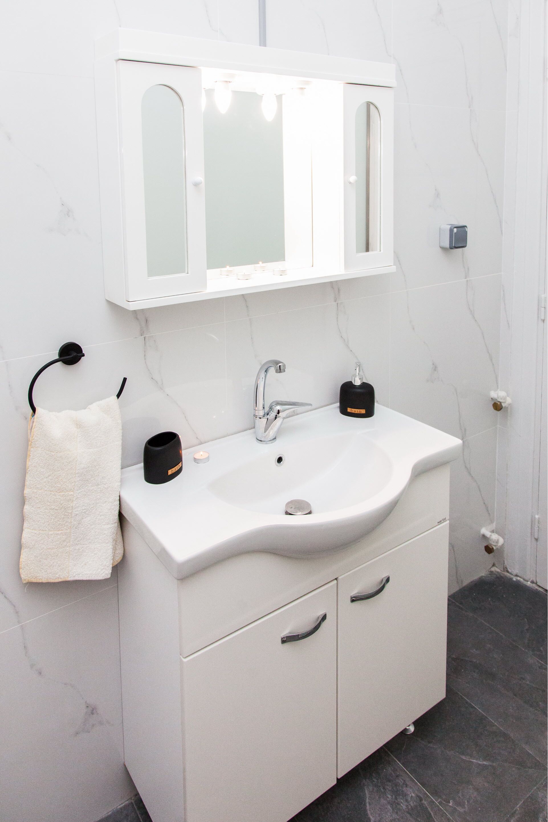 A bathroom with a white vanity, a mirror, a sink, and a towel rack.