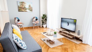 Uma sala de estar moderna com um sofá cinza, uma mesa de centro de madeira, uma televisão e uma planta em vaso.