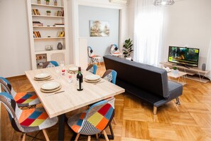 Een moderne woonkamer met een eettafel voor vier personen, een bank, een boekenkast en een televisie.