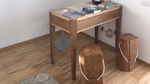 Ein Holztisch mit Zeitschriften und einer Lampe, zwei Holzschemeln und ein gerahmtes Kunstwerk an der Wand.