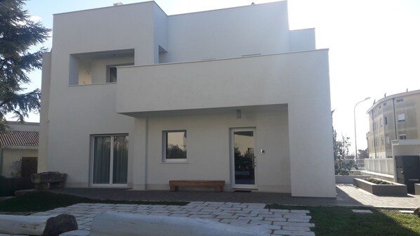 A modern two-story building with a flat roof, large windows, and a small front porch with a bench.