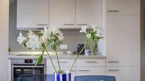 Eine moderne Küche mit weißen Schränken, einem blauen Stuhl und einem Tisch mit einer Vase mit weißen Blumen.