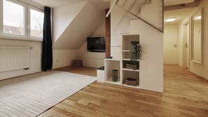 Ein moderner, gut beleuchteter Raum mit schrägverdeckter Decke, einem großen Fenster, einem Flachbildfernseher und eingelassenen Regalen mit dekorativen Gegenständen.