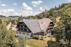 Ein großes, mehrstöckiges Gebäude mit einem geneigten Dach, umgeben von üppigem Grün und wolkenlosem Himmel.