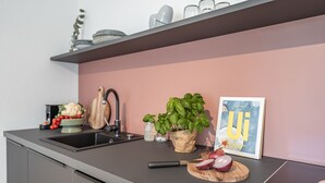 Una cocina moderna con encimera gris, un fregadero, una tabla de cortar con verduras, un cuchillo, una planta de albahaca en maceta y un cuadro enmarcado.