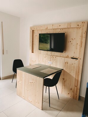 Une petite pièce moderne avec un mur en bois, un téléviseur à écran plat fixé au-dessus d’une table avec deux chaises, et une prise électrique sur le mur.