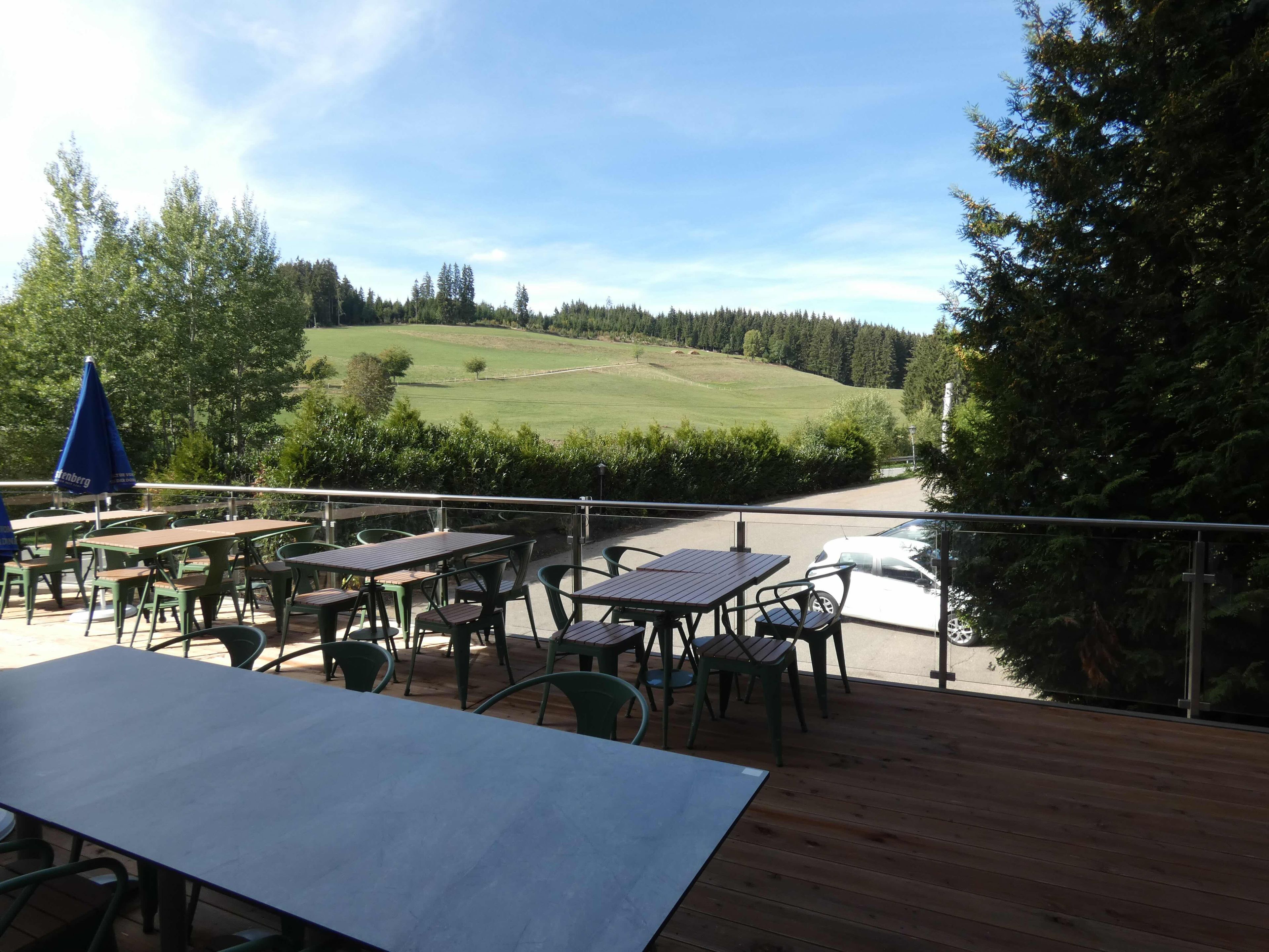 An outdoor seating area with tables and chairs, overlooking a green landscape and a road.