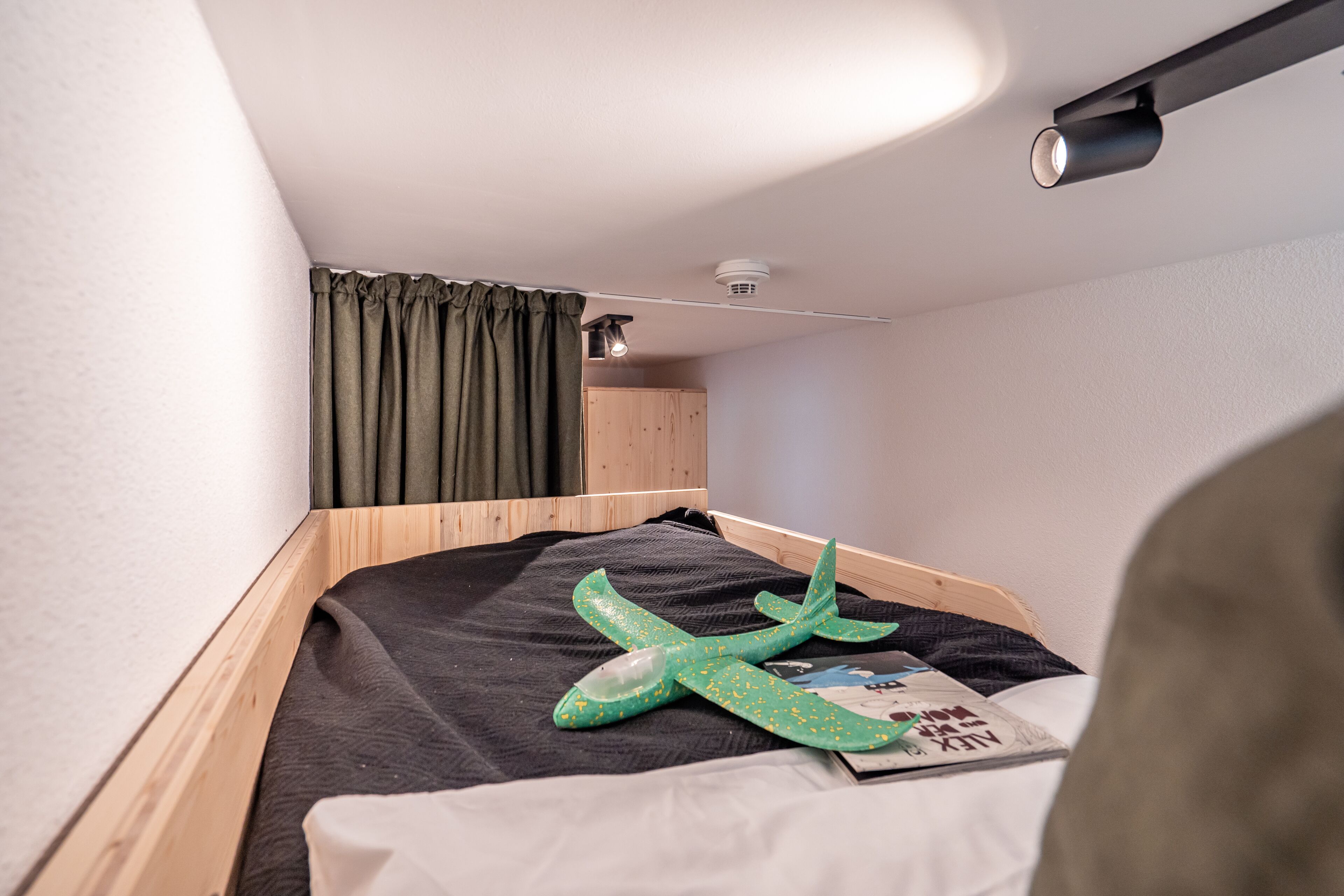 A small, neatly made bed with a dark blanket and a green airplane toy on it.