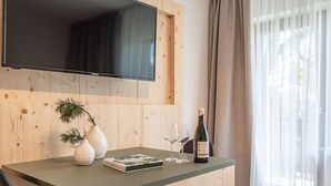 Un interior de madera con un televisor de pantalla plana montado en la pared, una pequeña mesa con un libro, dos jarrones, dos vasos y una botella de vino.