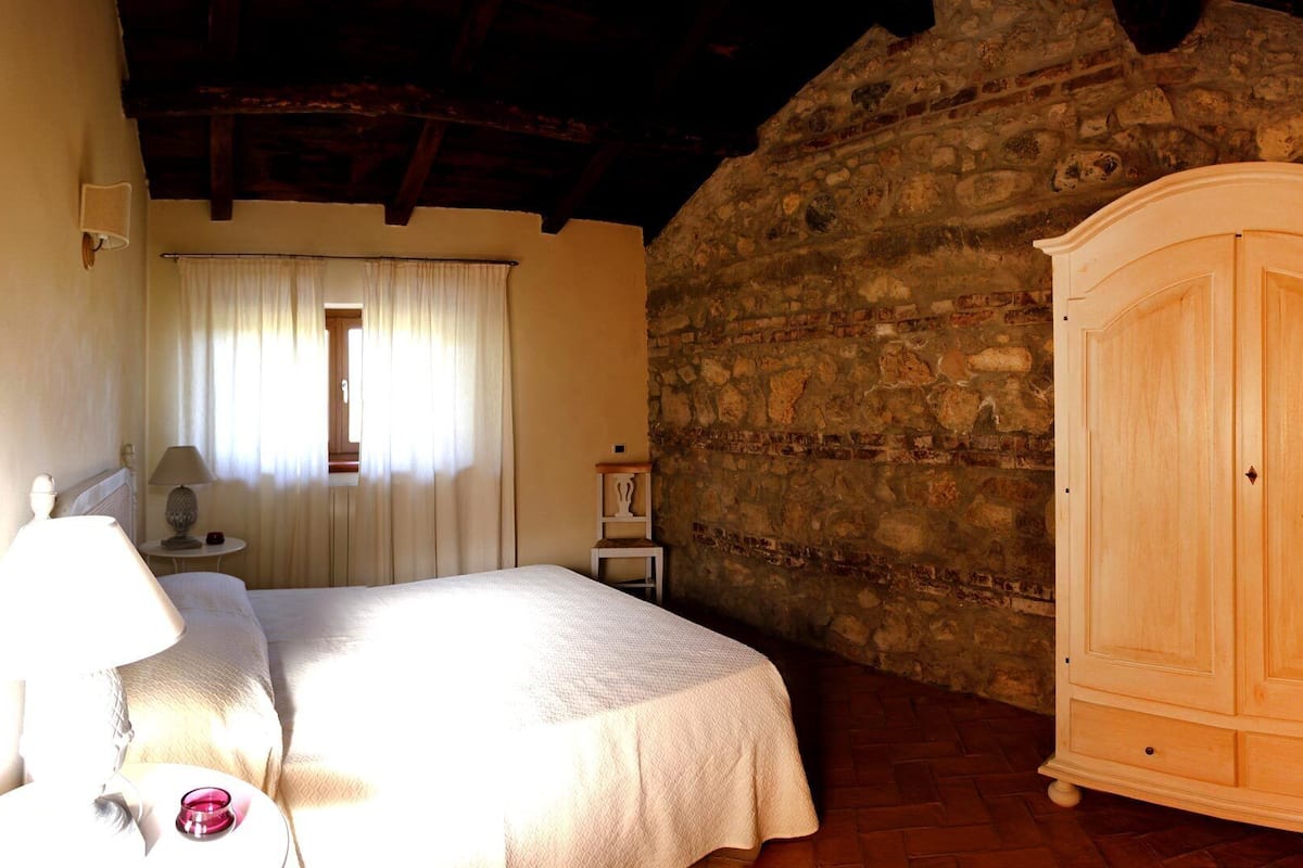Ein Schlafzimmer mit Bett, Nachttisch, Lampe, Kleiderschrank und einer Steinwand.