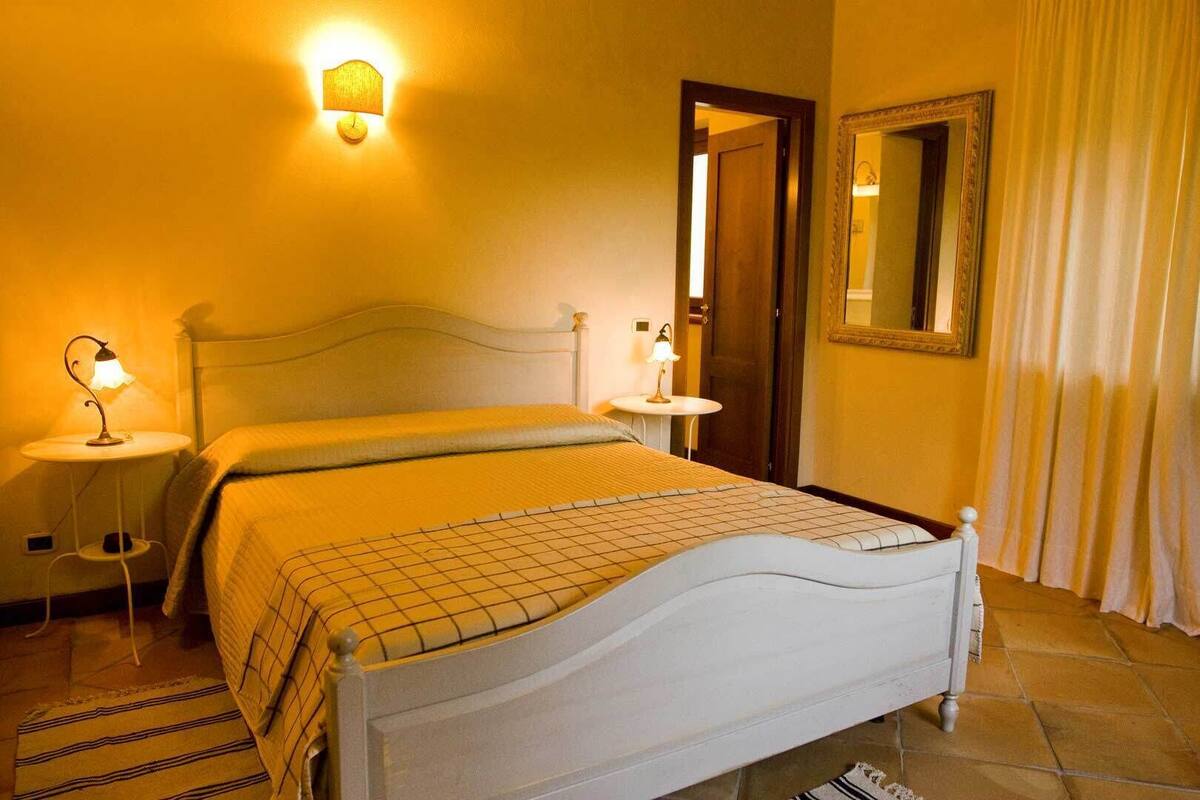 Ein ordentlich eingerichtetes Schlafzimmer mit Bett, Nachttischlampen, einem runden Tisch, einem Spiegel und einer Tür.