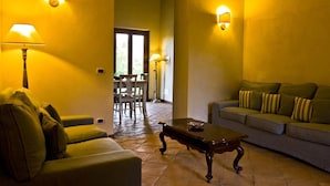 A living room with a sofa, a coffee table, and two lamps. There is a dining table with chairs in the background. - Borgo Serafino (Paterno Calabro)