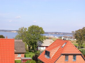 A residential area with houses featuring red-tiled roofs, a large tree, and a view of a body of water in the background. - Ferienhäuser Zum Höft 44 (Mönchgut-Granitz)