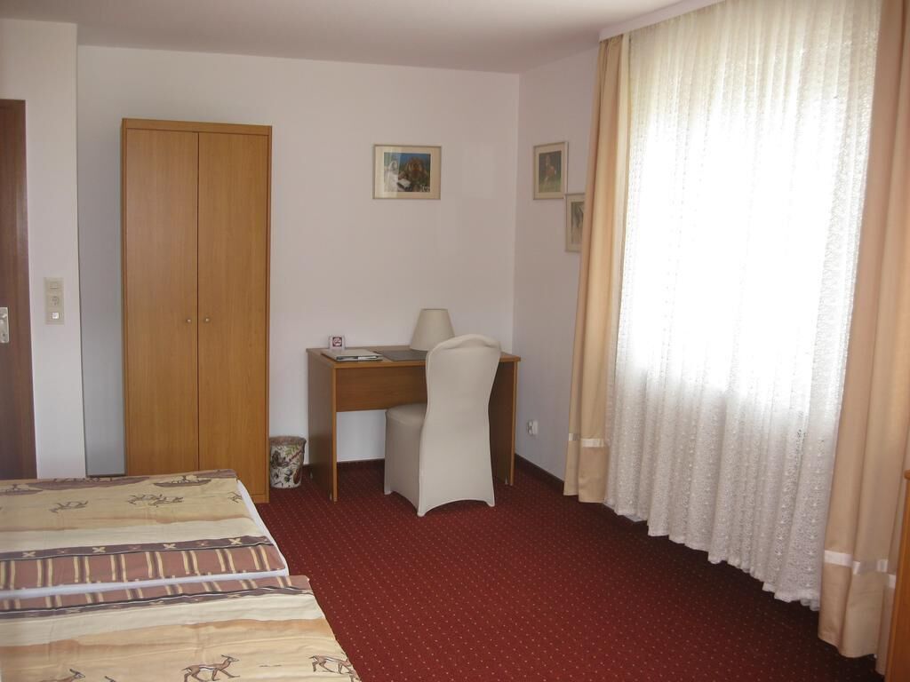 A hotel room with a bed, a desk, a chair, a wardrobe, and curtains.