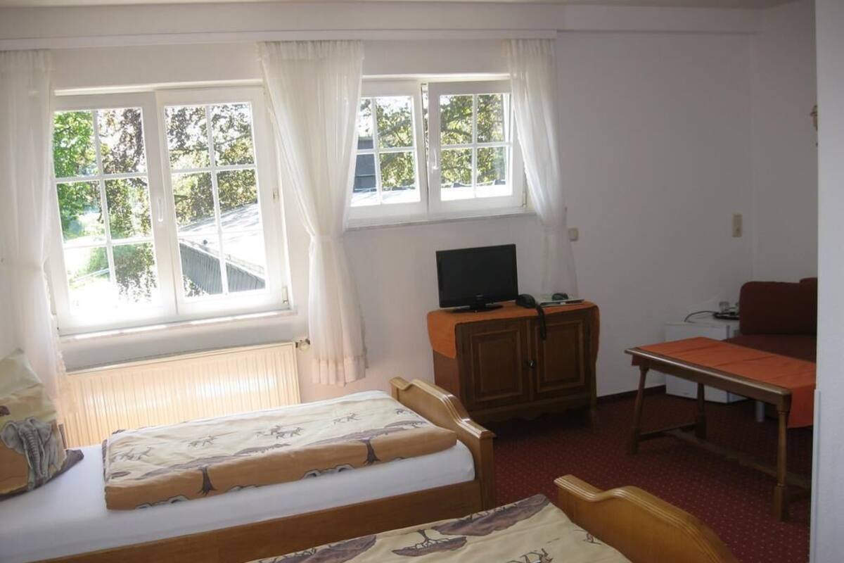 Una habitación con dos camas individuales, un escritorio de madera con una silla, un televisor y una ventana con cortinas.