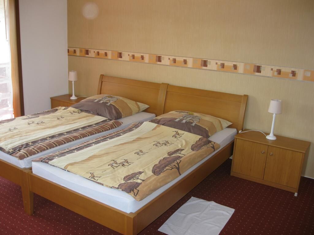 Una cama doble con una colcha estampada, un cabecero de madera, una mesita de noche con lámpara y un pequeño mueble de madera.