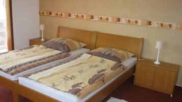 Una cama doble con una colcha estampada, un cabecero de madera, una mesita de noche con lámpara y un pequeño mueble de madera.