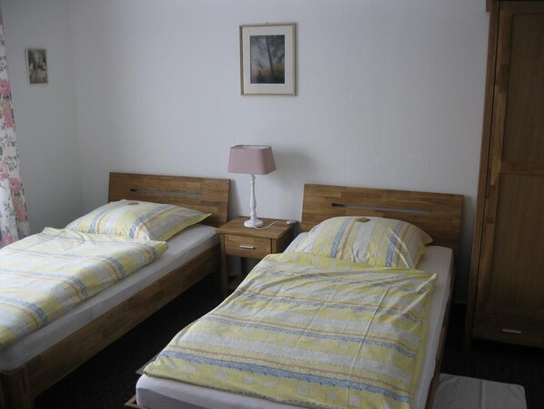 A room with two single beds, a bedside table with a lamp, and a wooden wardrobe.
