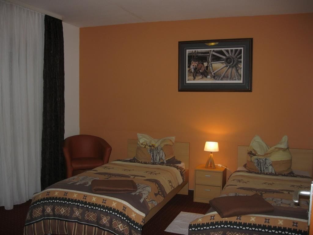 A hotel room with two beds, a chair, a nightstand with a lamp, and a framed picture on the wall.