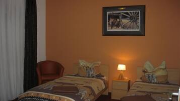 A hotel room with two beds, a chair, a nightstand with a lamp, and a framed picture on the wall.