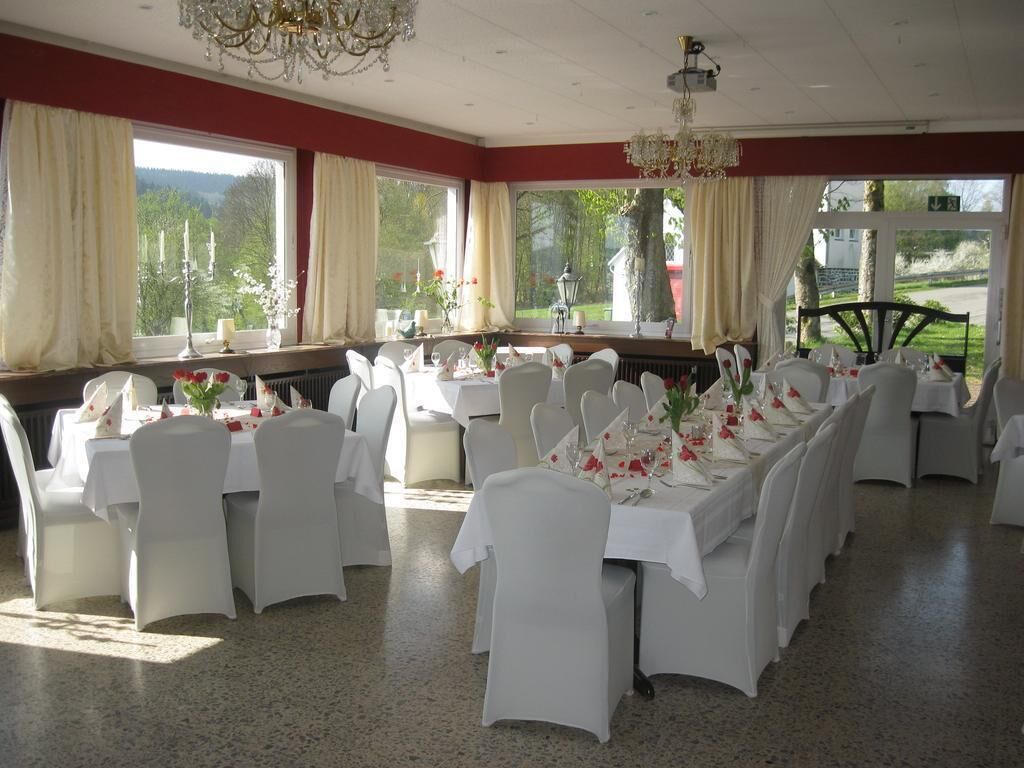 A dining area with multiple tables set for a formal event, large windows with curtains, and a chandelier.