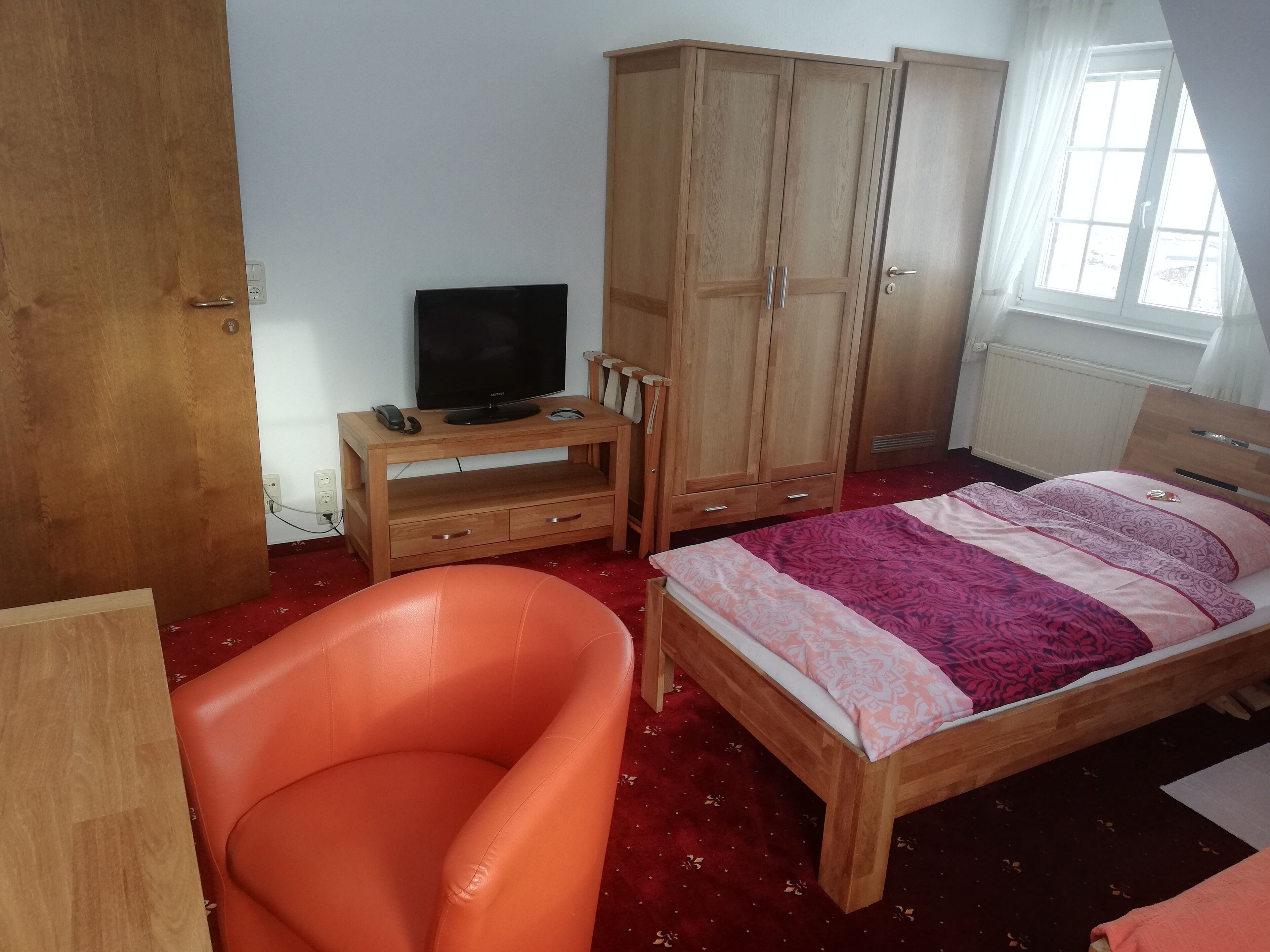 Un dormitorio con cama de madera, armario de madera, mesita de noche con televisión y una silla roja.