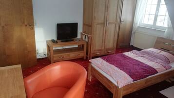 Un dormitorio con cama de madera, armario de madera, mesita de noche con televisión y una silla roja.