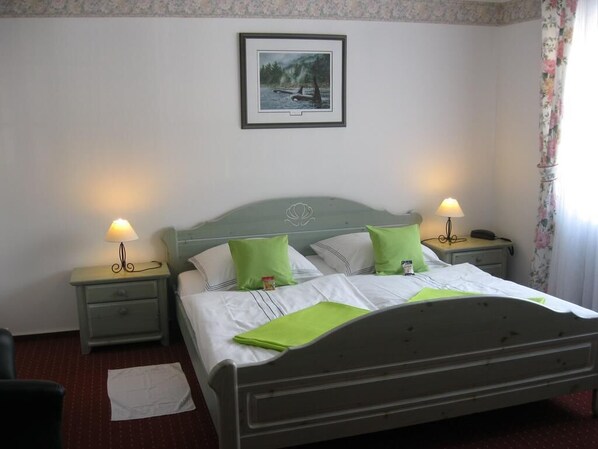 A neatly made bed with green pillows, a framed picture on the wall, and a lamp on each side.