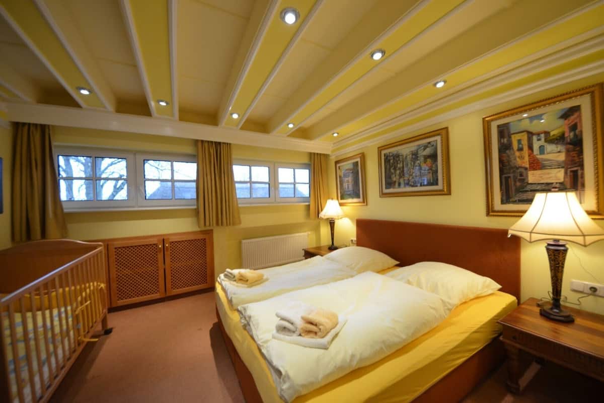 A hotel room with two beds, a crib, a window with curtains, and artwork on the walls.
