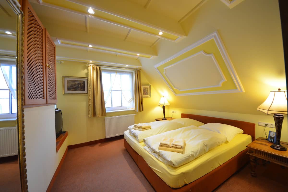 A hotel room with two beds, a wooden headboard, a window with curtains, a radiator, and a lamp on a bedside table.
