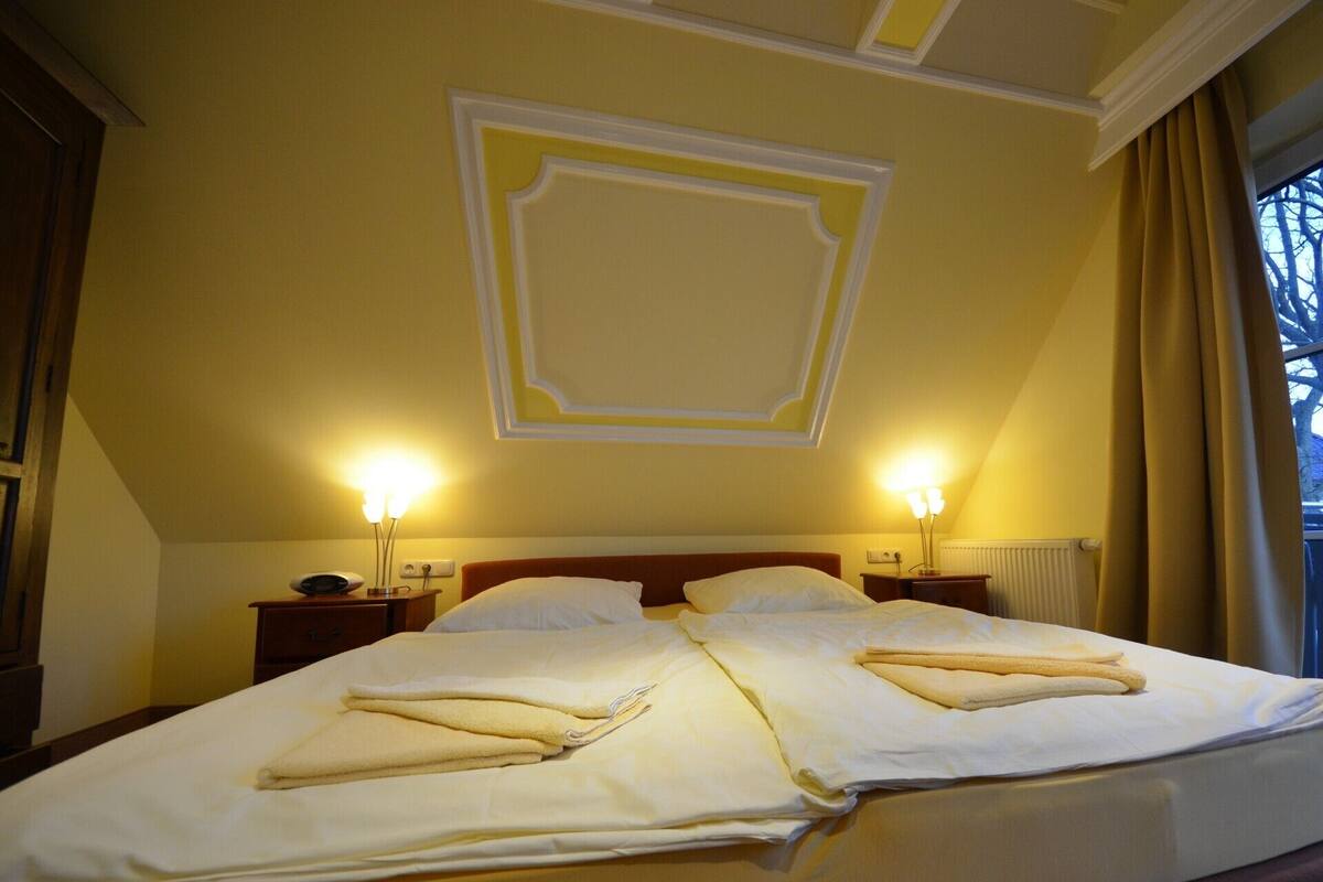 A hotel room with a large bed, two bedside lamps, and a decorative ceiling panel.