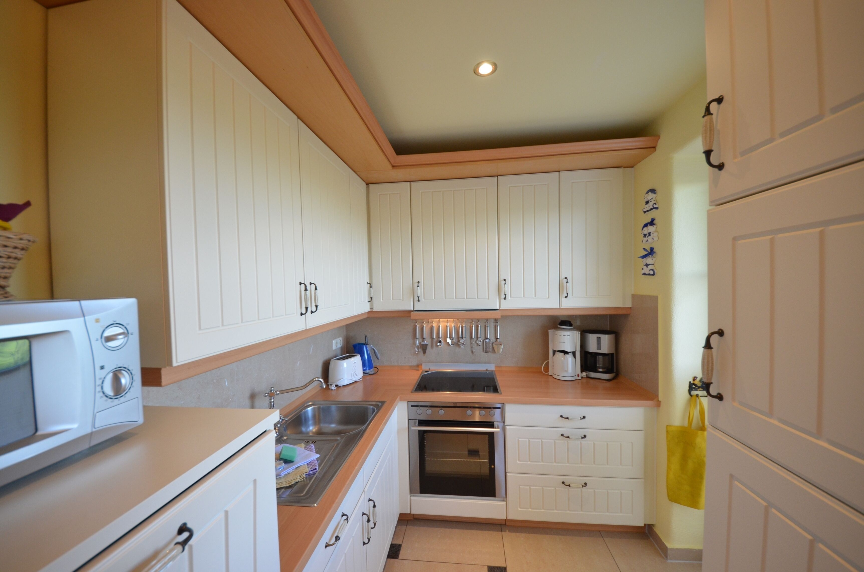 Una cocina compacta con armarios blancos, microondas, lavamanos y cafetera.