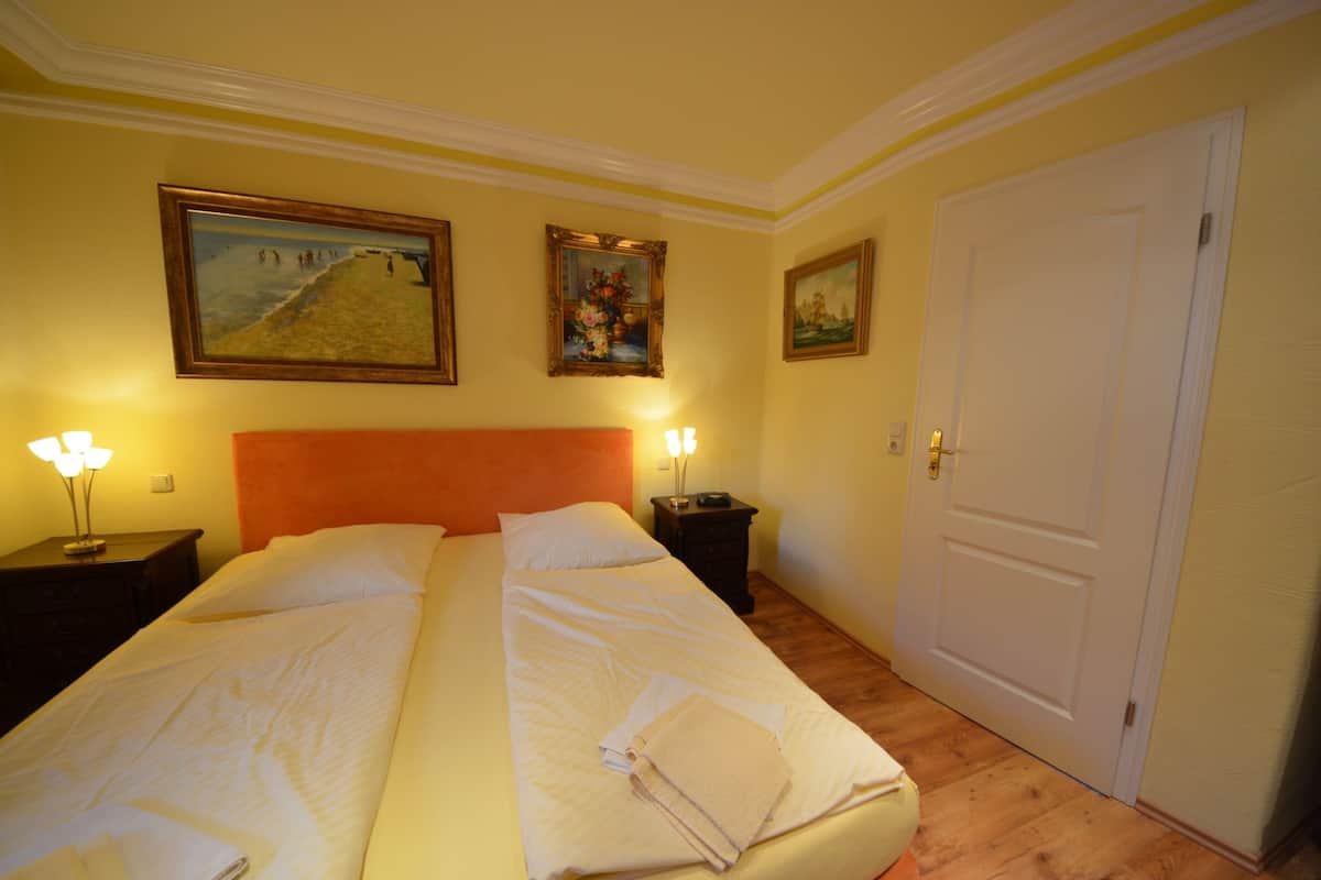 A double bed with white linens, two bedside tables with lamps, and three framed artworks on the wall.