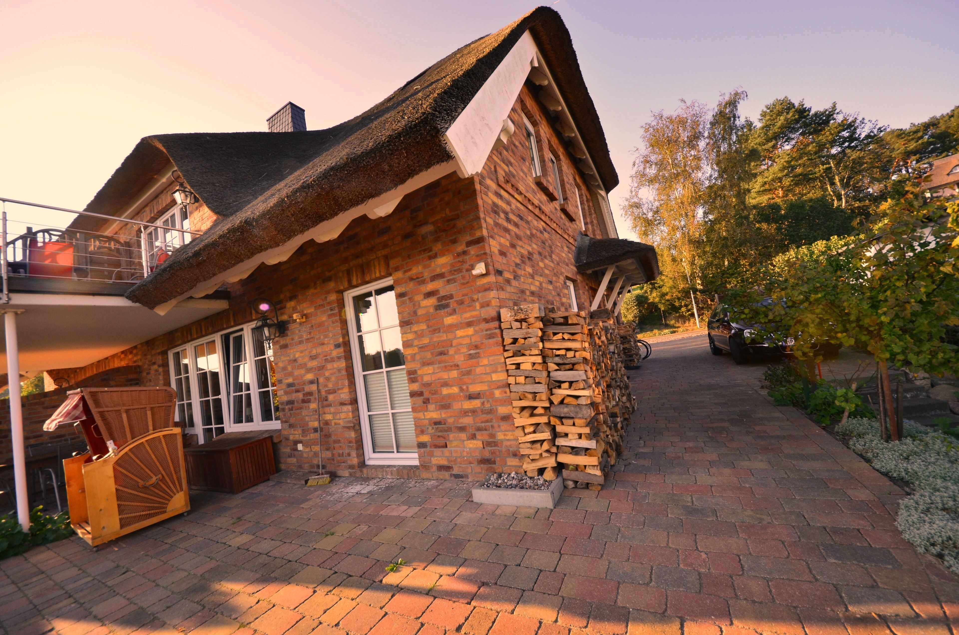A brick house with a thatched roof, a wooden bench, and a stack of firewood.