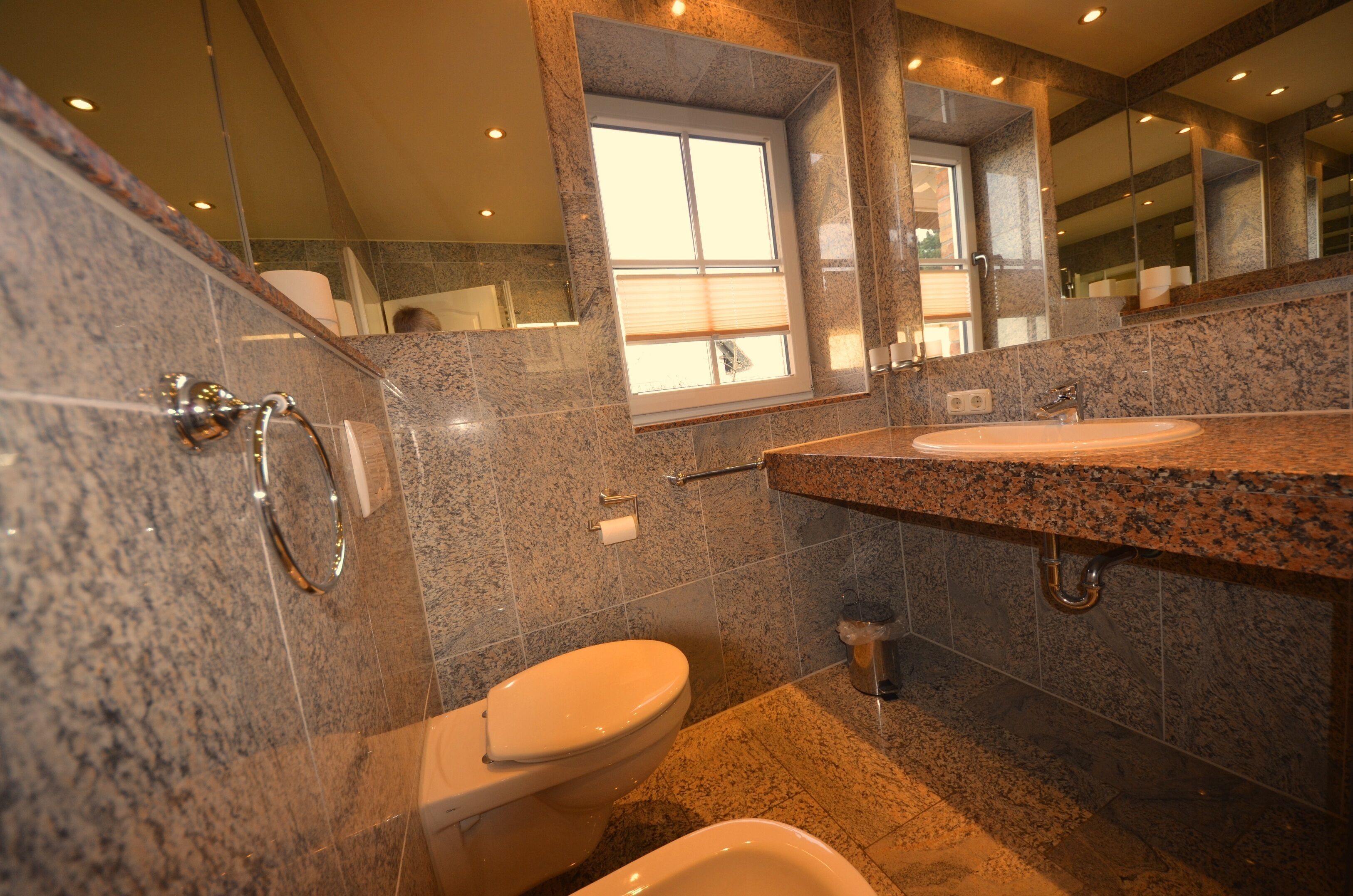 A modern bathroom with granite countertops, a toilet, and a bidet.