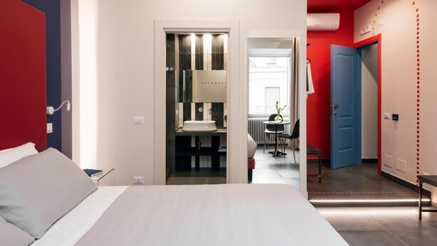 Une chambre d’hôtel moderne comprenant un lit, une salle de bain avec un miroir et un lavabo, ainsi qu’un petit coin salon avec une table et des chaises.