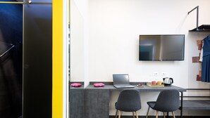 Une cuisine moderne avec un plan de travail gris, deux chaises noires, un ordinateur portable et un téléviseur à écran plat fixé au mur.