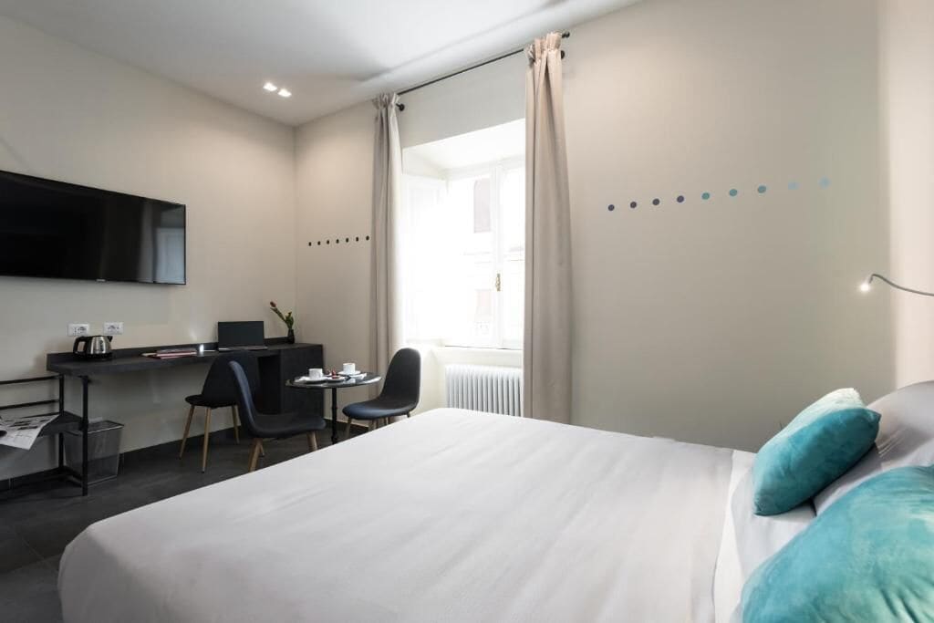 Habitación de hotel con cama, escritorio, silla, televisor y ventana con cortinas.
