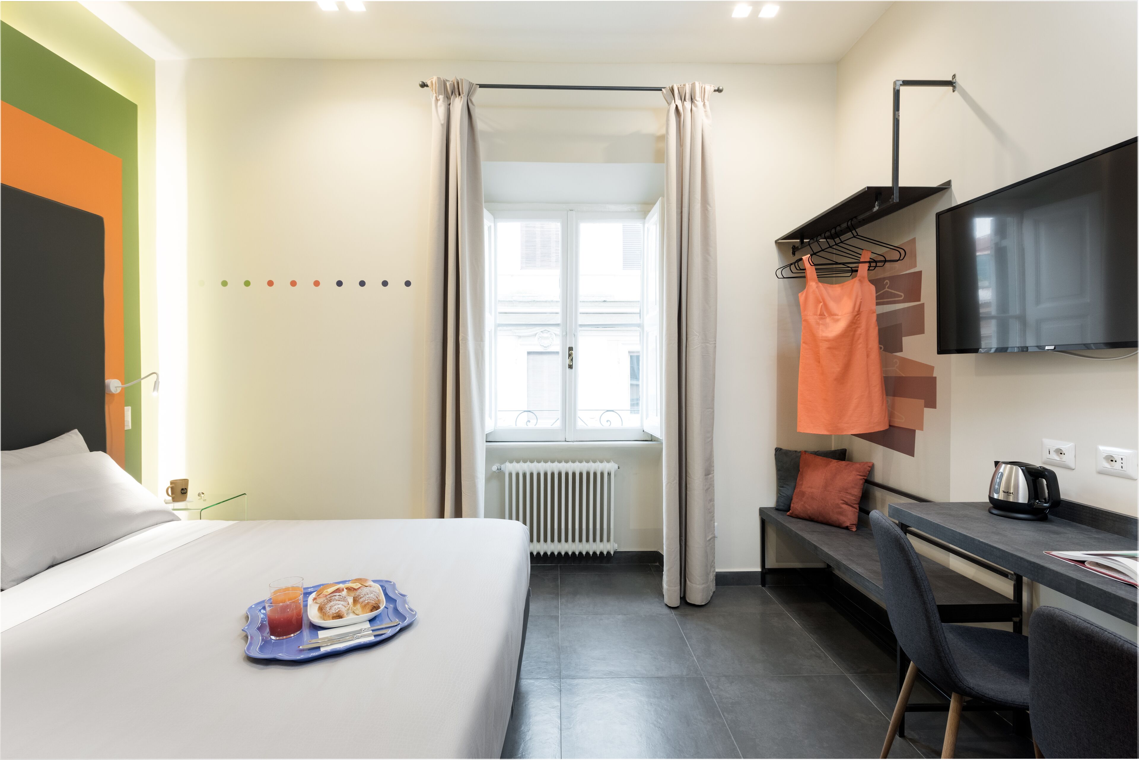 Ein Hotelzimmer mit Bett, Schreibtisch, Fernseher und einem Fenster mit Vorhängen.