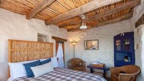 Ein gemütliches Schlafzimmer mit einem hölzernen Kopfteil, einer karierten Bettdecke, Korbstühlen, einem kleinen Tisch und einem blauen Schrank.