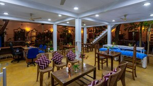 Un vaste espace intérieur aménagé avec différents types de sièges, notamment des tables et des chaises, et un escalier menant à un niveau supérieur.