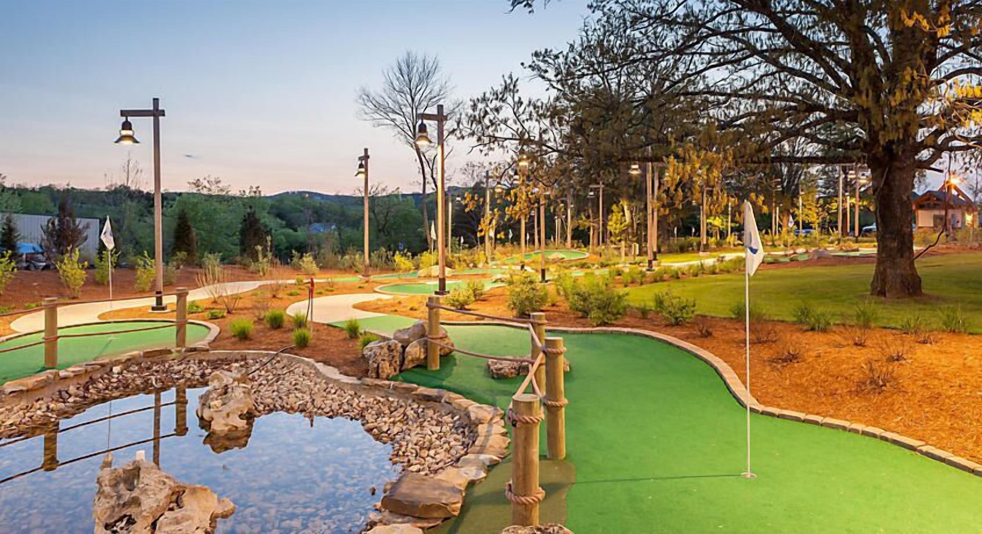 A miniature golf course with a pond, green fairways, and wooden structures.