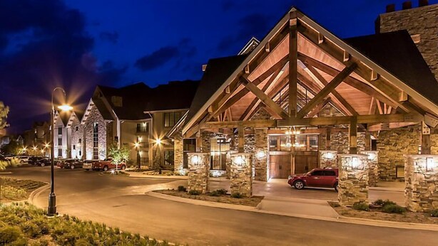 Eine Lodge mit einer Steinfassade, Holzbalken und einem roten Auto vor der Tür.