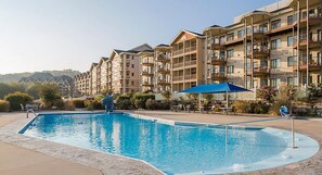 A swimming pool with a blue umbrella, surrounded by multi-story buildings with balconies and outdoor seating. - Amazing Paradise Point Resort in Hollister! (Hollister)