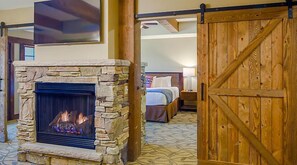A stone fireplace with a fire, a bed with a wooden headboard, and a wooden barn-style door.