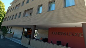 Un bâtiment moderne doté d’un toit plat et d’une enseigne rouge sur laquelle on peut lire « OCHSEN LODGE ».