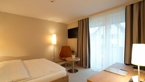 Une chambre d’hôtel avec un lit, un bureau, une chaise, une petite table avec une plante et un téléviseur fixé au mur.